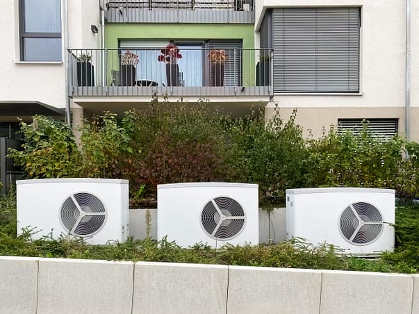 Wärmepumpe Eigentumswohnung nachrüsten Foto: Drei nachgerüstete Wärmepumpen für Eigentumswohnungen vor einem Mehrfamilienhaus