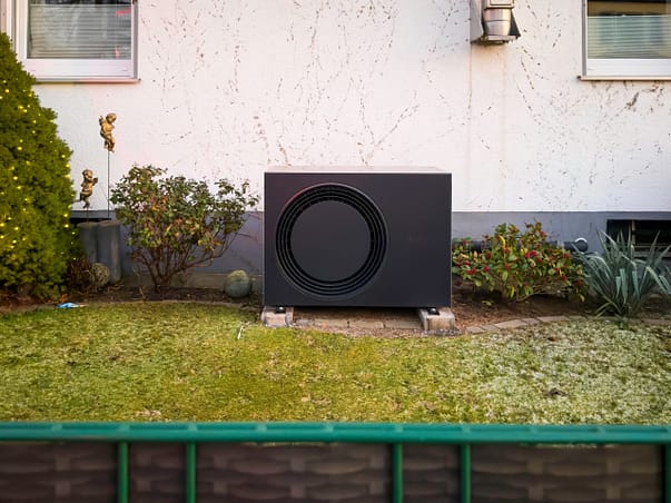 fehlerfreie Auslegung der Wärmepumpe Eine schwarze Wärmepumpe mit korrekter Auslegung im Vorgarten vor einer Hausfassade
